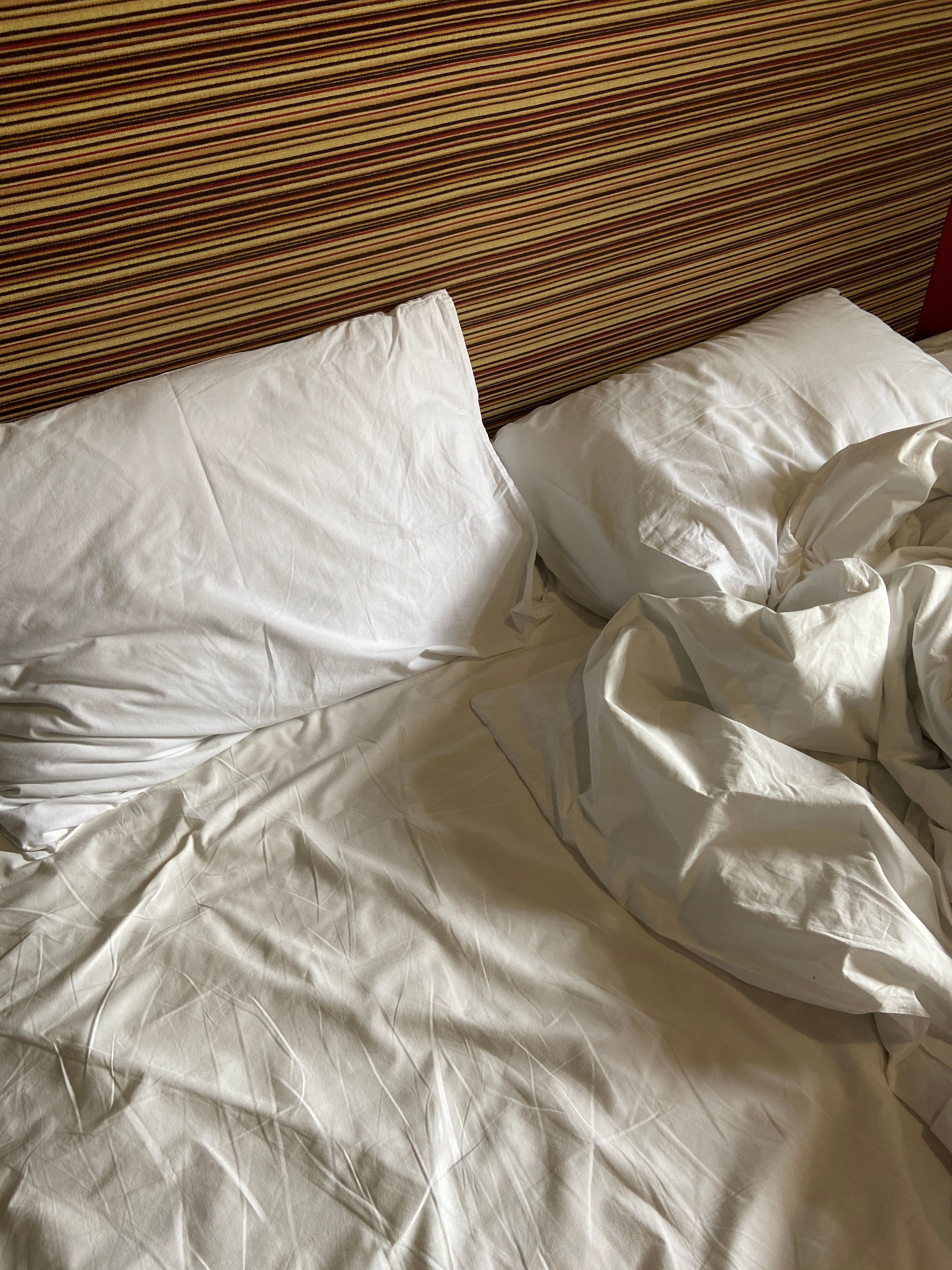 Unmade bed with white linens, a common sight when checking for bed bugs during anxious nighttime inspections